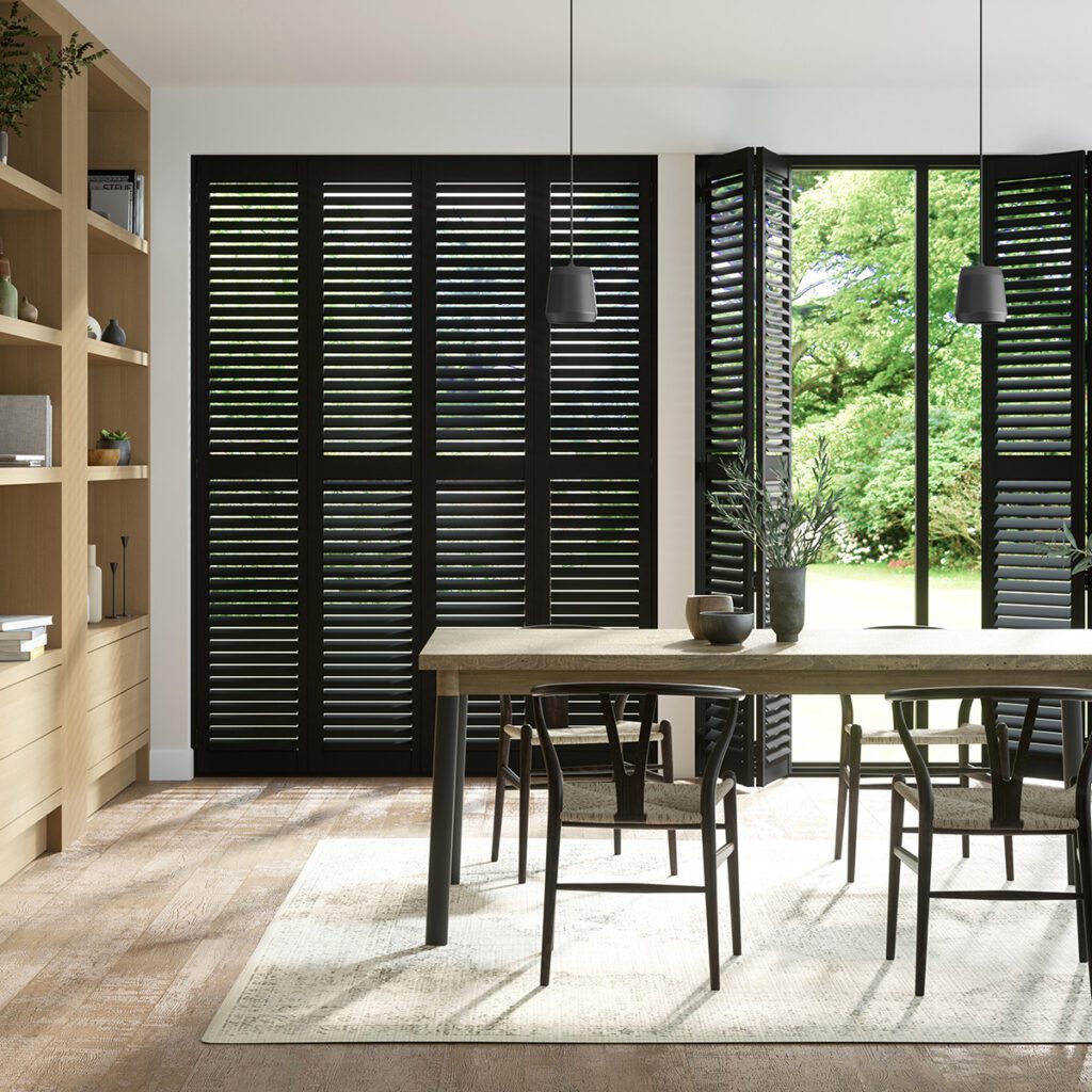 Image shows a dining room interior with black plantation shutters covering the windows and doors. 