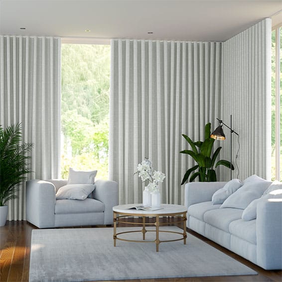 Image shows a living room with floor to ceiling blockout s-fold curtains that cover all the windows right into the corner.