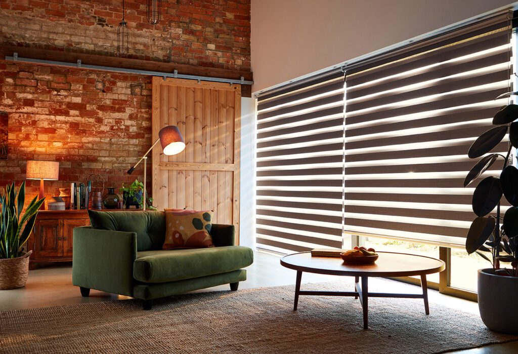 Zebra blinds can be automated on our Tuiss SmartView app. Image shows zebra blinds in an industrial interior with an exposed brick wall and barn door. 