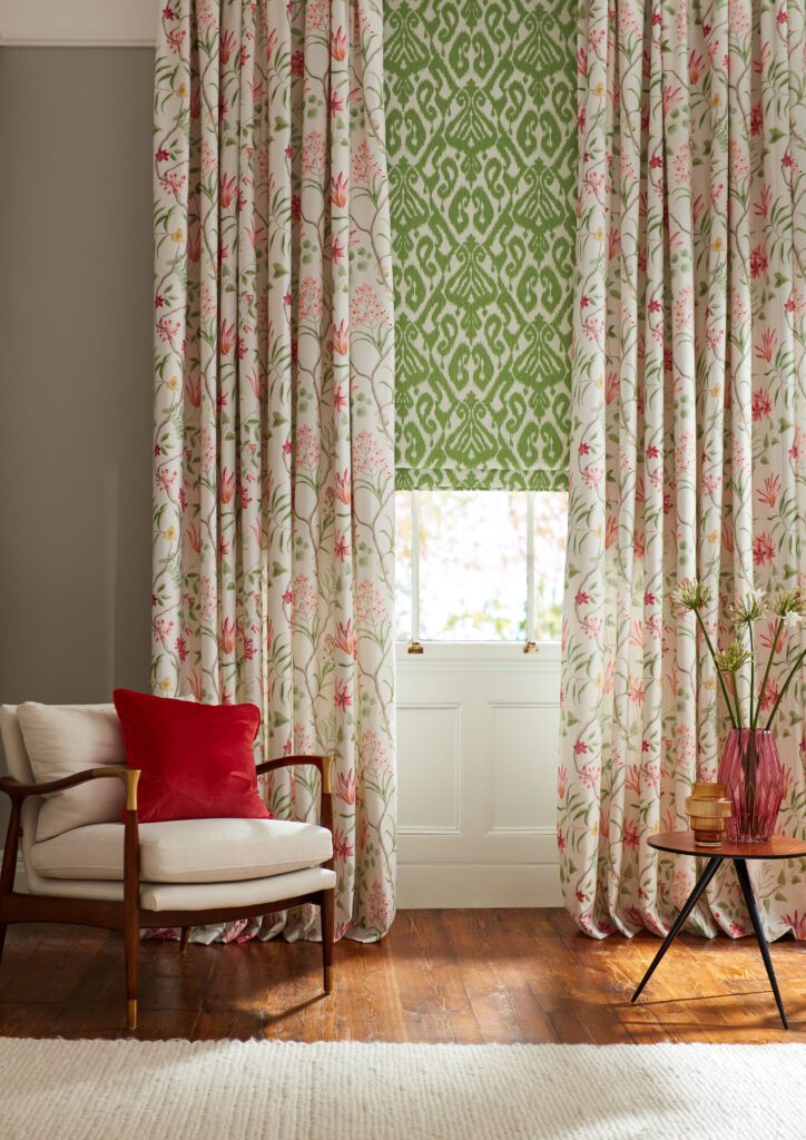 Contemporary sitting room with a mid-century modern armchair in front of a window. The window features a roman blind in a green ikat fabric, layered with a floral curtain. 